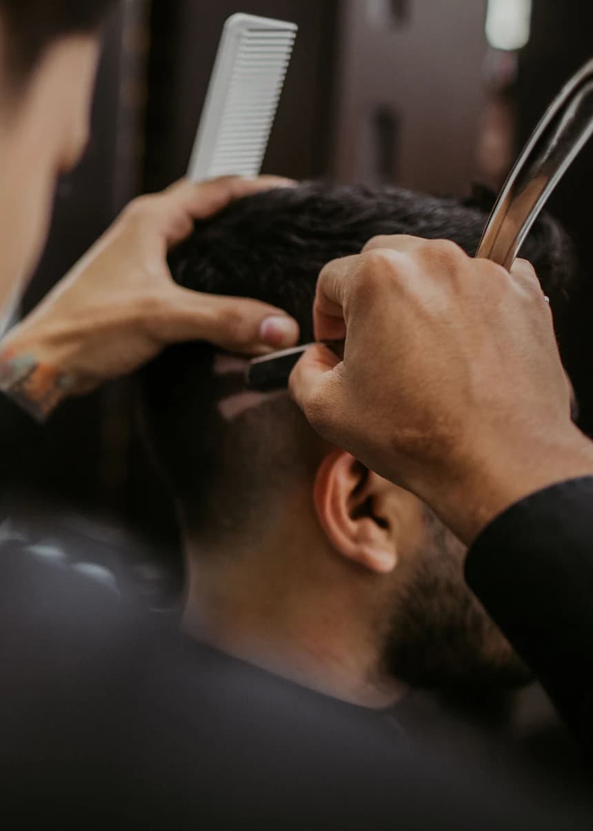 Barbeiro fazendo o acabamento do corte de um cliente com pente e navalha